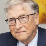 older smiling white man (Bill Gates) with short gray hair, glasses, and a suit.