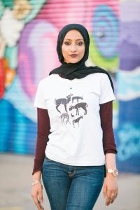 woman wearing a black hijab, a maroon long sleeve shirt under a white graphic t-shirt, and blue jeans