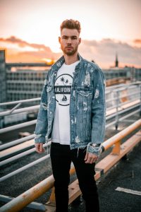 Man wearing black jeans with a white graphic t-shirt and a blue distressed denim jacket