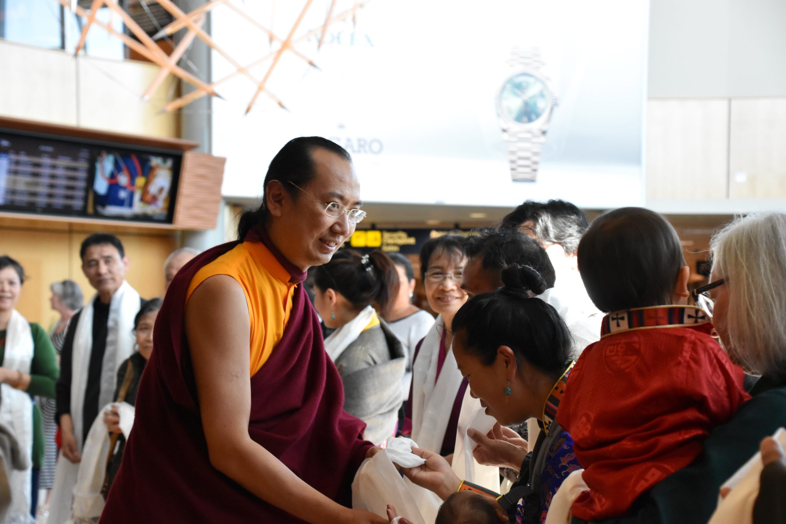 Buddhist teacher dressed in red and orange greeting people.