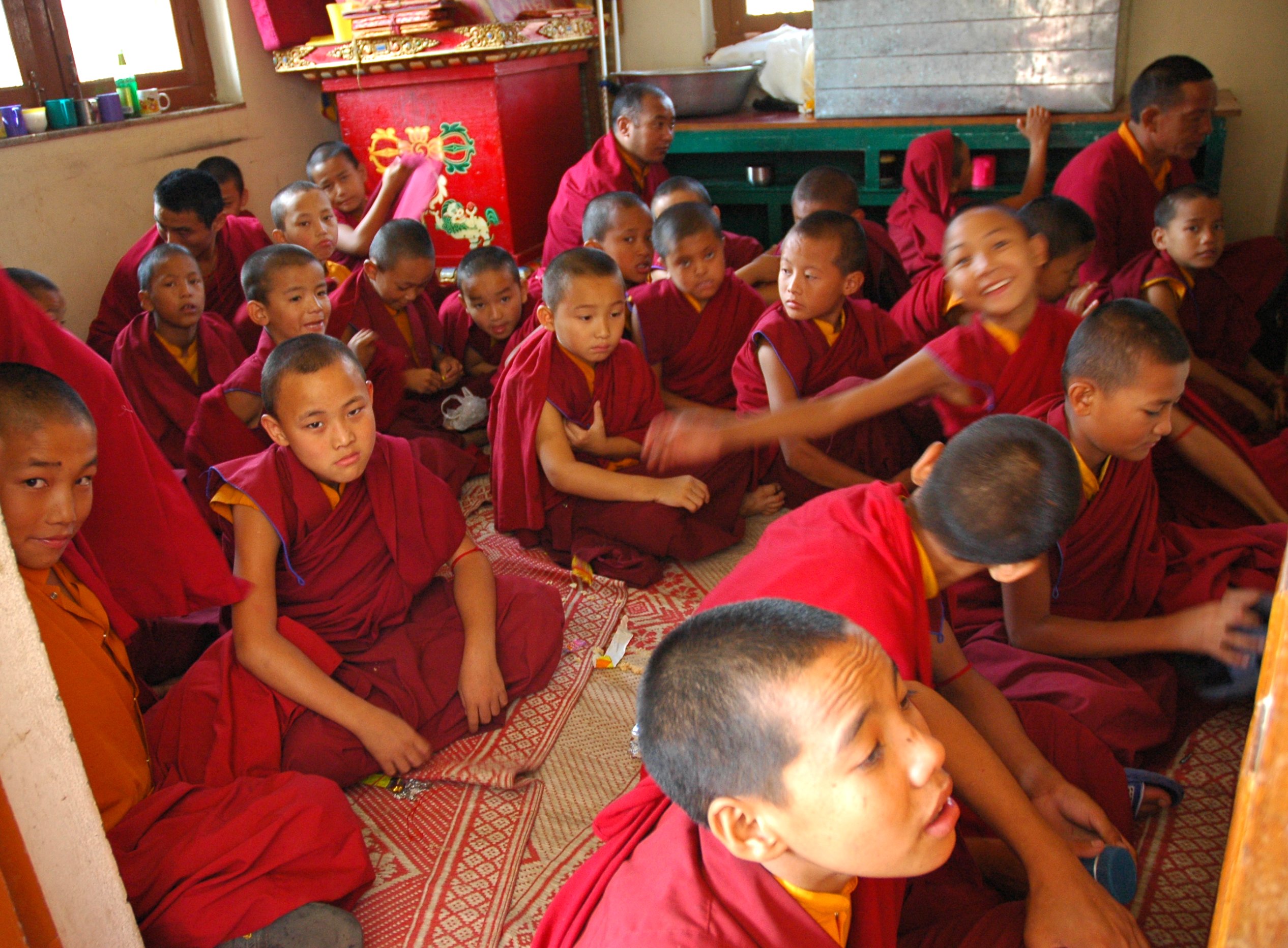 Tibetan children dressed in orange and red sitting on the rug-covered floor