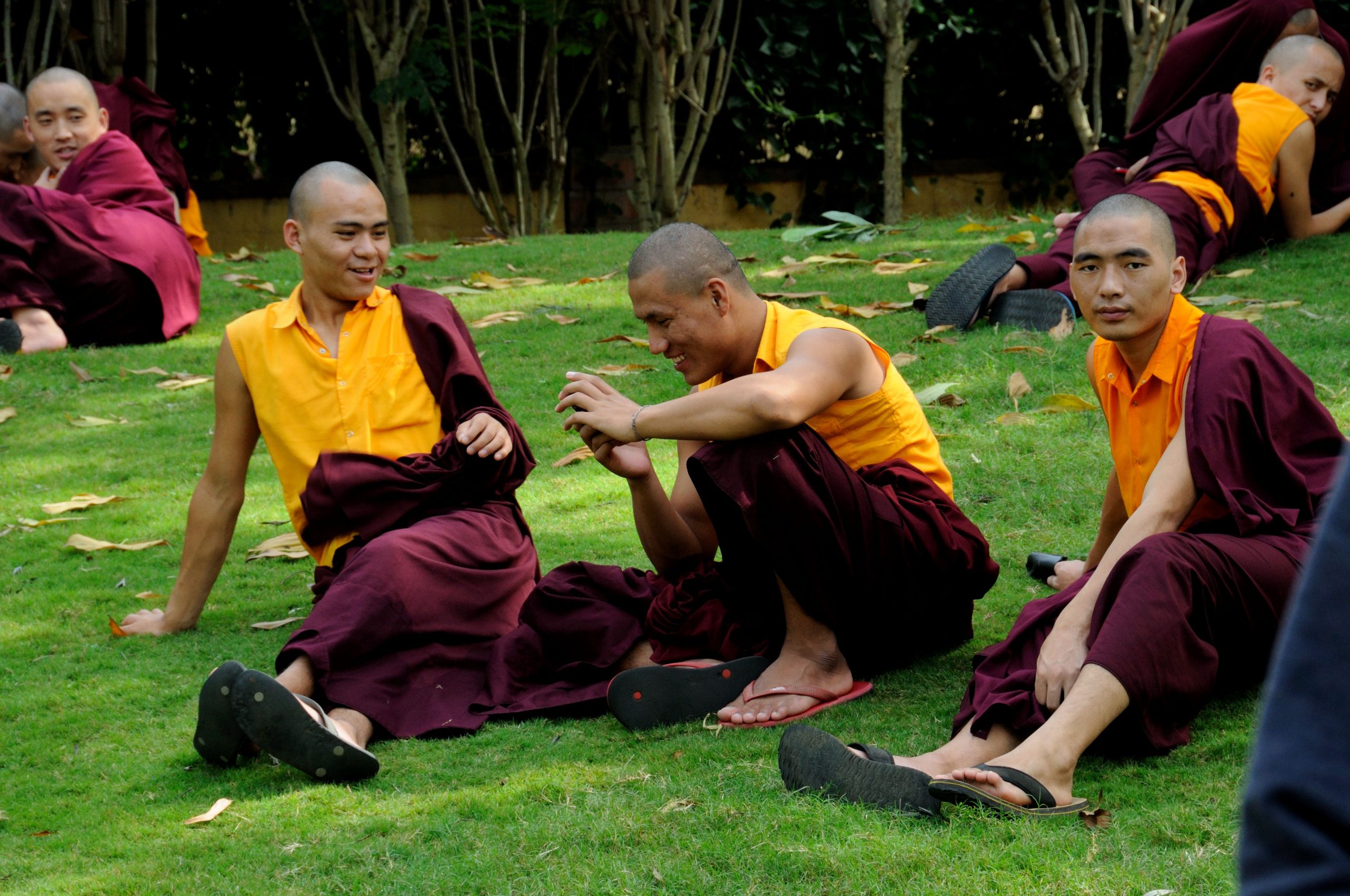 teenage boys in orange and red traditional clothing with shaved heads sitting on a hill of green grass and smiling