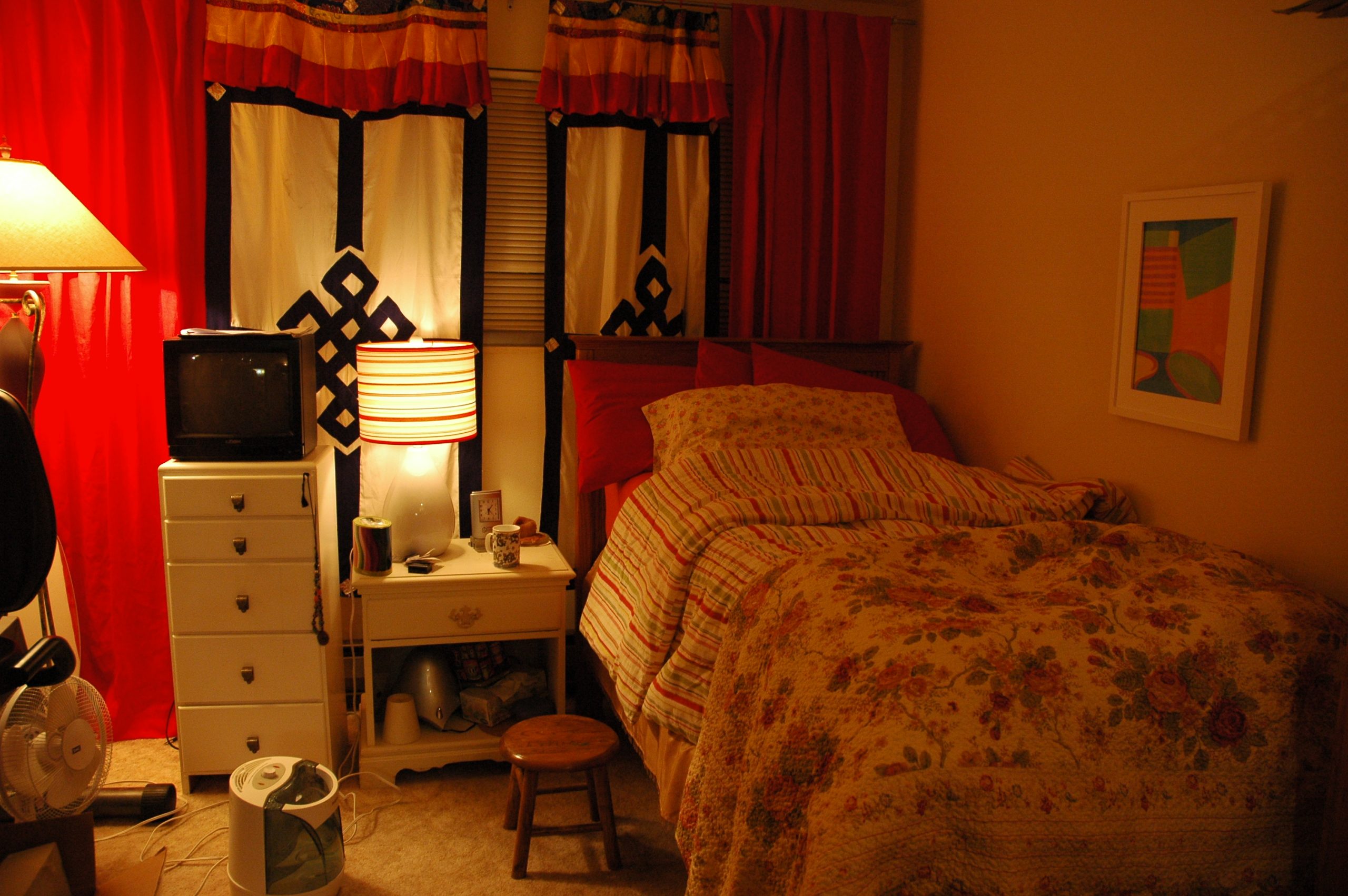 Teen bedroom with dim lighting, red and white and black decorations, a box tv, and curtains with the Buddhist endless knot pattern