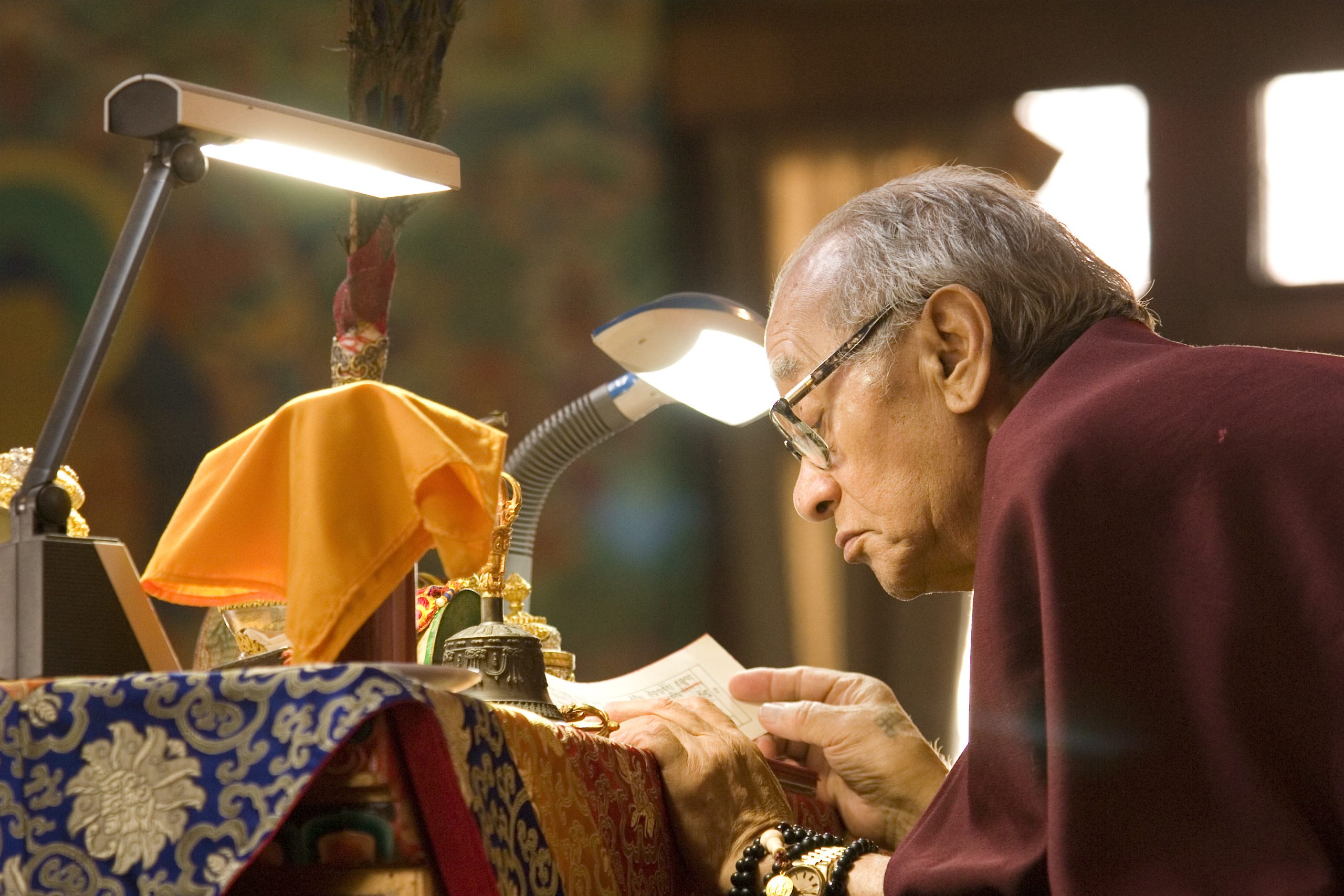 Monk reading under lamps on a table covered with ornamental cloth