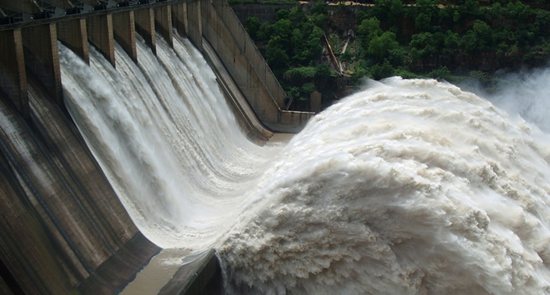 A large volume of water gushes out of the gates of a dam at a hydroelectric facility.