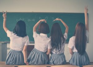 four girls in a classroom making hand signs to the board