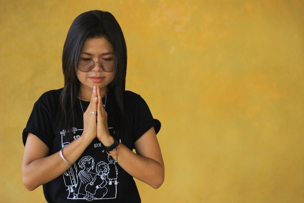 A woman greeting with her two hands raised and put together as if in prayer and the head is bowed.