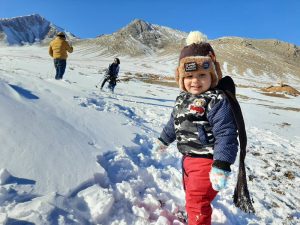 Imageo f a 2 years old boy standing playing with snow with a mountain in background