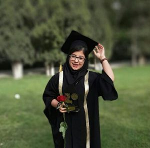 iranian girl taking picture on her graduation day. she is earing black gown and cap, holding red rose and her diploma on her hand.