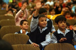 young children with school uniform on raising hands